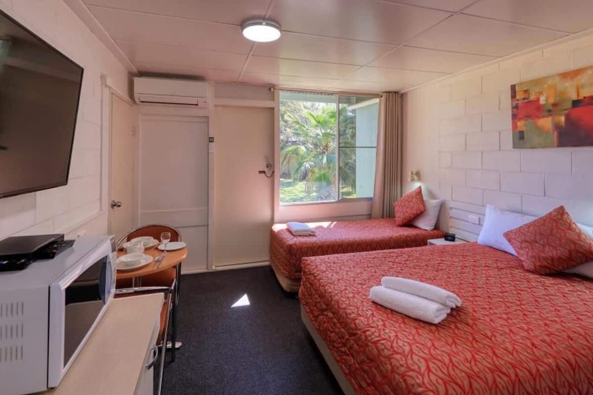 A hotel room with two beds, a TV, a desk with a chair, and a window with a view of greenery.