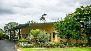 A building with a covered entrance, surrounded by a well-maintained garden with various plants and flowers. - Motel Carnarvon (Roma)
