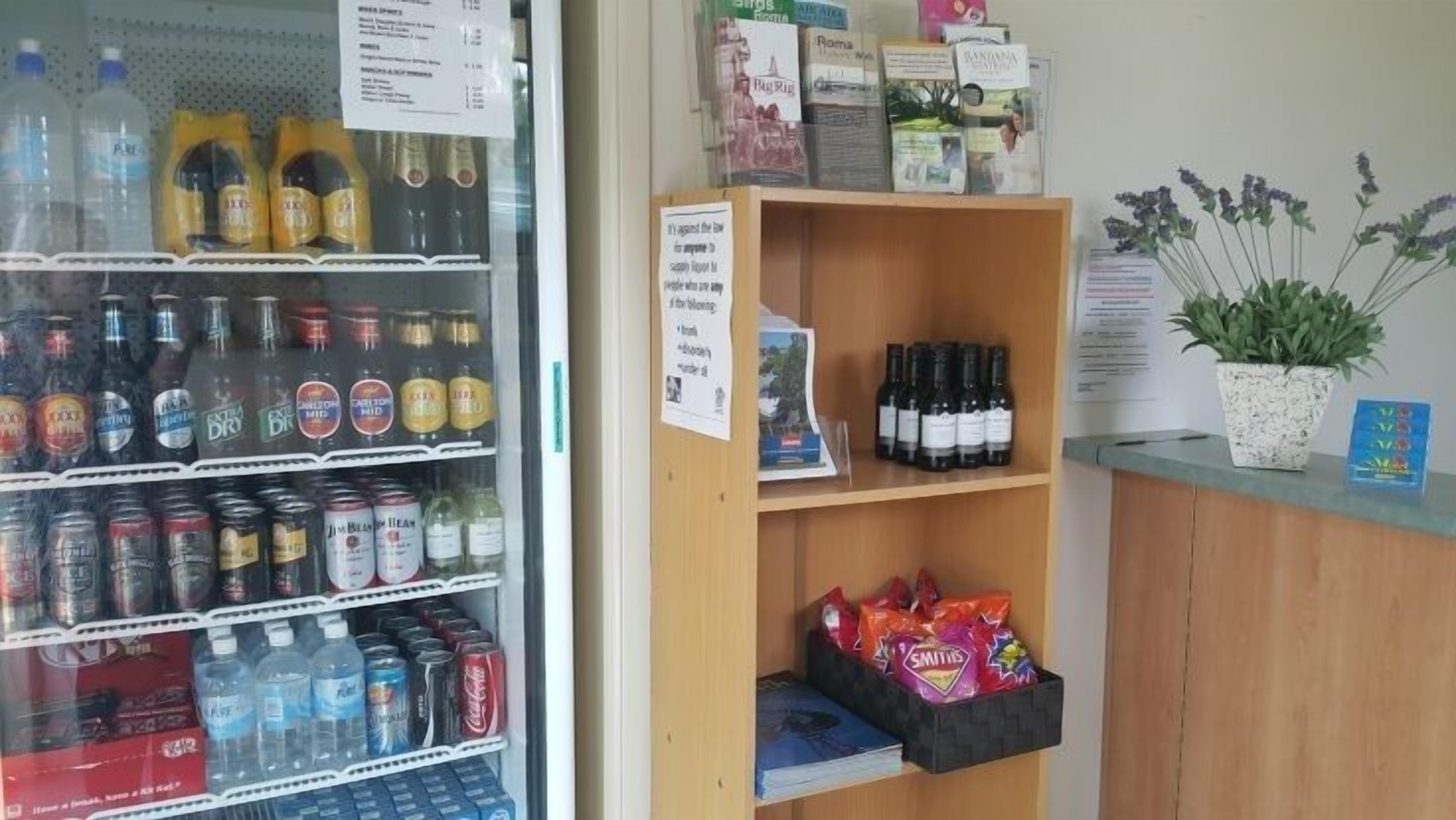 Un refrigerador lleno de bebidas variadas, una estantería con botellas de vino y una presentación de aperitivos.