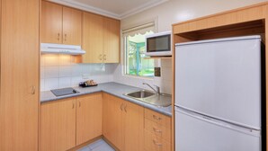 A compact kitchen with wooden cabinets, a built-in microwave, a stainless steel sink, and a white refrigerator. - Motel Carnarvon (Roma)