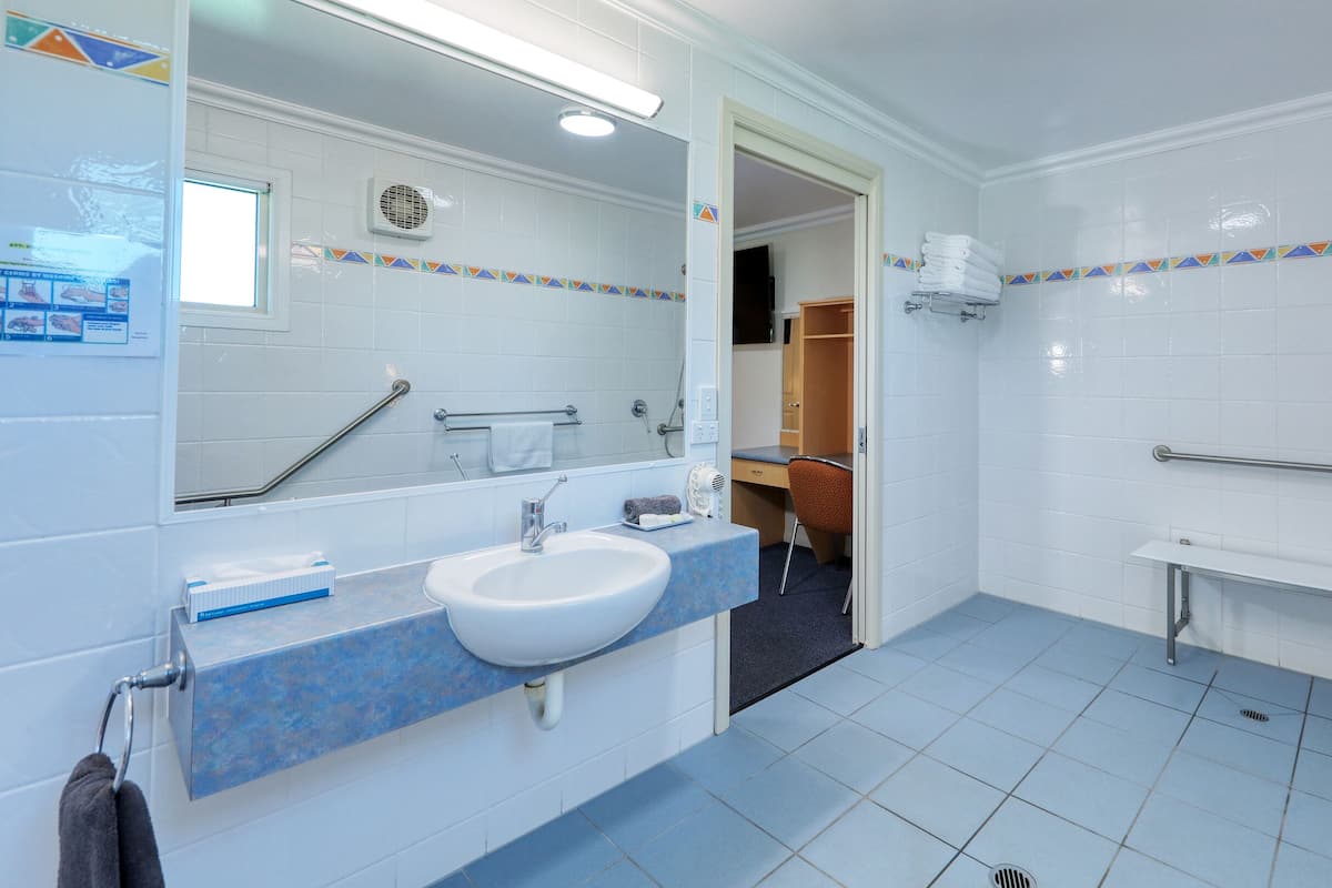 A bathroom with a sink, mirror, shower, and a small desk with a chair.
