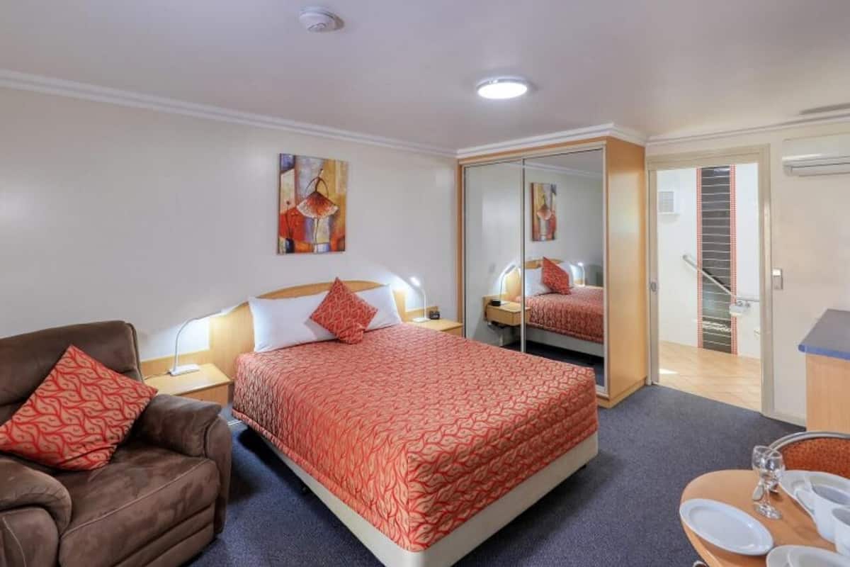 A hotel room with a bed, a chair, a desk, a mirror, and a door leading to a staircase.