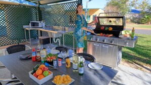 An outdoor barbecue setup with a grill, dining table, and various food and drink items. - Motel Carnarvon (Roma)