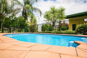 Una piscina con borde de baldosas, rodeada por una valla y palmeras.