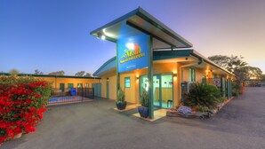 A motel with a reception area, a parking lot, and a well-maintained garden with red flowers. - Motel Carnarvon (Roma)