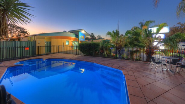 A swimming pool with a tiled deck, a fenced area, and a building with a sign that reads "Hotel". - Motel Carnarvon (Roma)