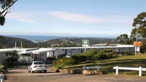 A caravan park with a white caravan, a paved driveway, and a sign indicating a 24-hour service area. - Kingfisher Motel (Merimbula)