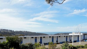 A row of white motel rooms with blue doors, a 'VACANCY' sign, and a view of the landscape. - Kingfisher Motel (Merimbula)