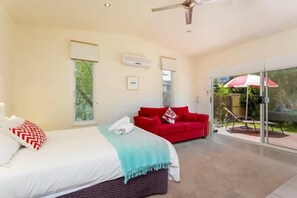 A modern hotel room with a bed, a red sofa, and a sliding glass door leading to a balcony. - Springtide Studio Apartments (Point Lonsdale)