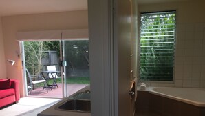 Eine moderne Küche mit Spüle, ein Essbereich mit einem roten Sofa und Blick auf einen Garten durch eine Schiebetür.
