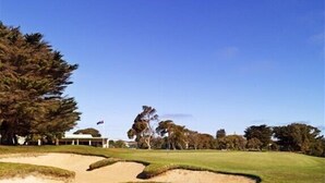 Ein Golfplatz mit Sandbunkern, einem Clubhaus und Bäumen im Hintergrund.