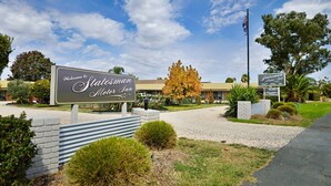 A Statesman Motel Inn sign with a welcoming message, a flag, and a well-maintained lawn. - Statesman Motor Inn (Corowa)