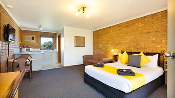 A hotel room with a bed, a desk, a chair, a kitchenette, and a brick wall.