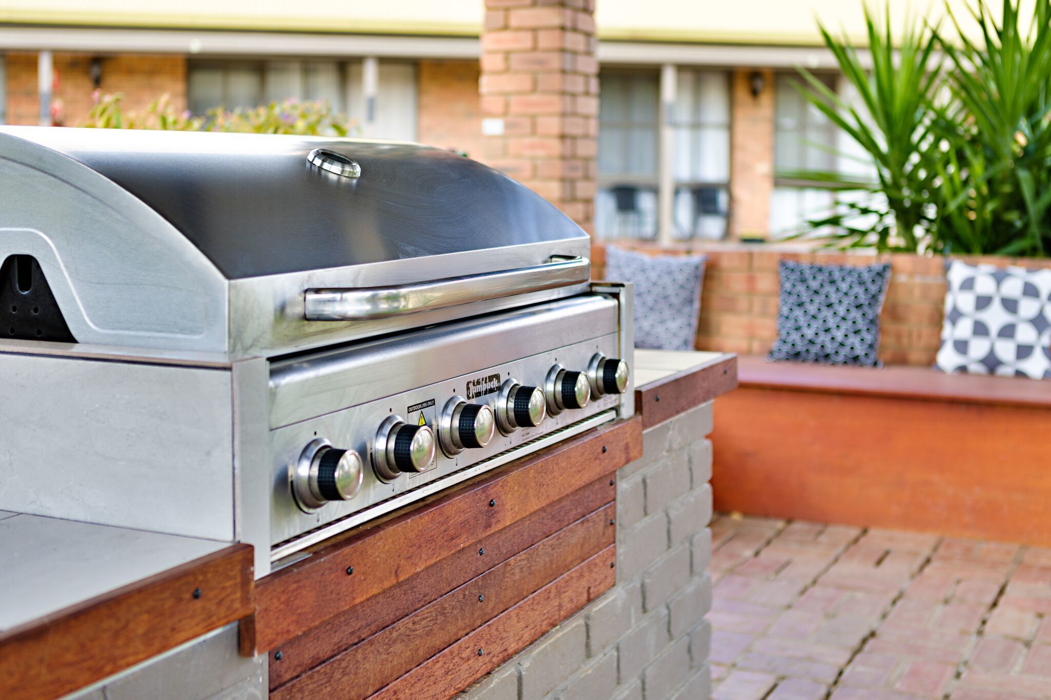A stainless steel barbecue grill with a hood, built into a brick and wood structure.