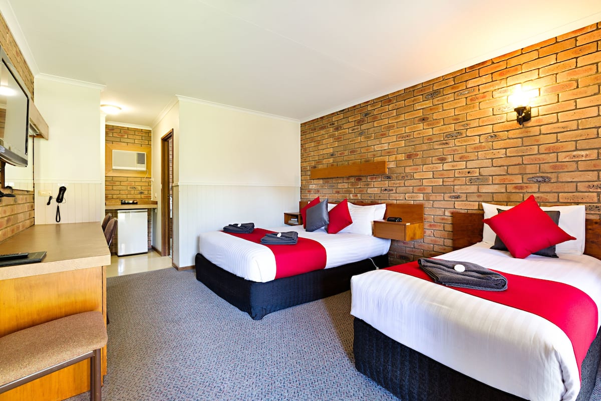 A hotel room with two beds, a desk, and a brick wall.