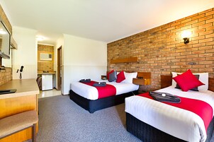 Quarto de hotel com duas camas, uma escrivaninha e uma parede de tijolos.