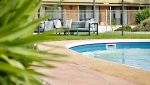 A swimming pool with a tiled edge, surrounded by a brick pathway. In the background, there is a fenced outdoor seating area with a sofa and cushions. - Statesman Motor Inn (Corowa)