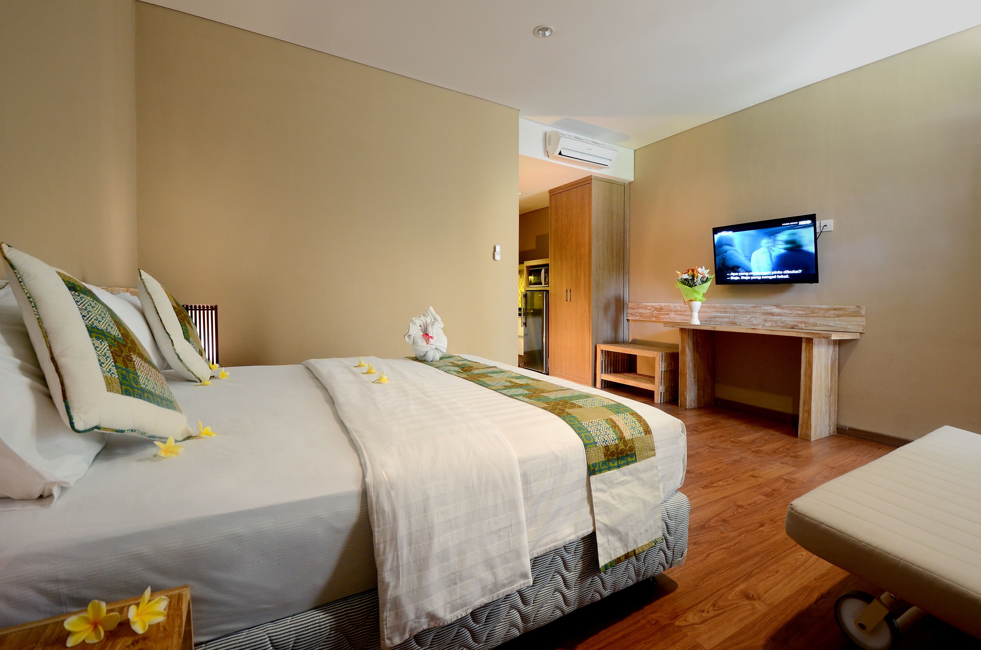 A hotel room with a large bed, a small desk, a television, and an air conditioning unit.