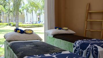 Two single beds with blue and white bedspreads and yellow flower pillows, overlooking a serene outdoor area with palm trees and lounge chairs.