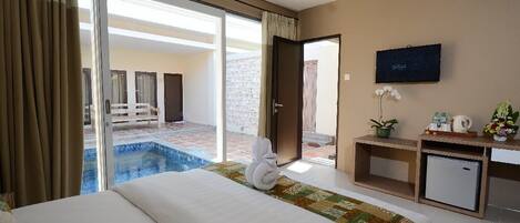 A hotel room with a bed, a small desk, a television, and a view of an outdoor swimming pool.