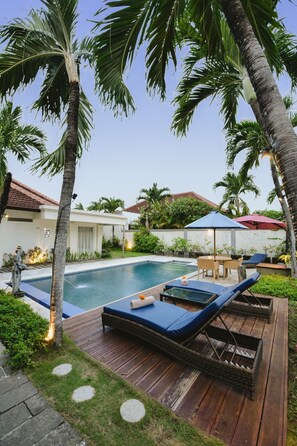 A pool area with lounge chairs, a wooden deck, and palm trees. - Bali Breezz Hotel (Jimbaran)