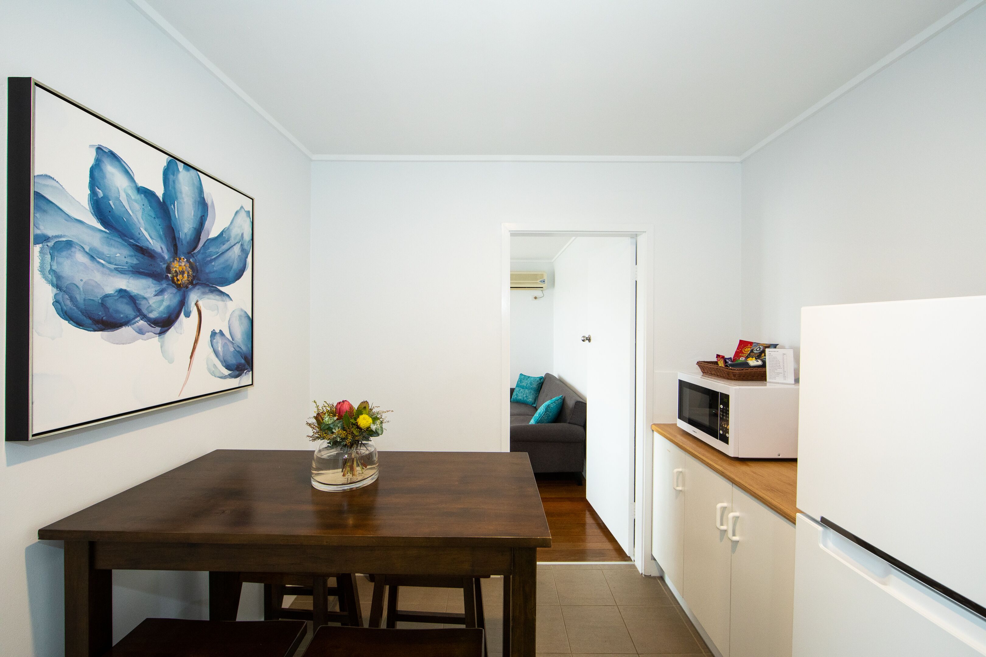 A compact kitchen with a wooden table, white cabinets, and a microwave on the countertop.