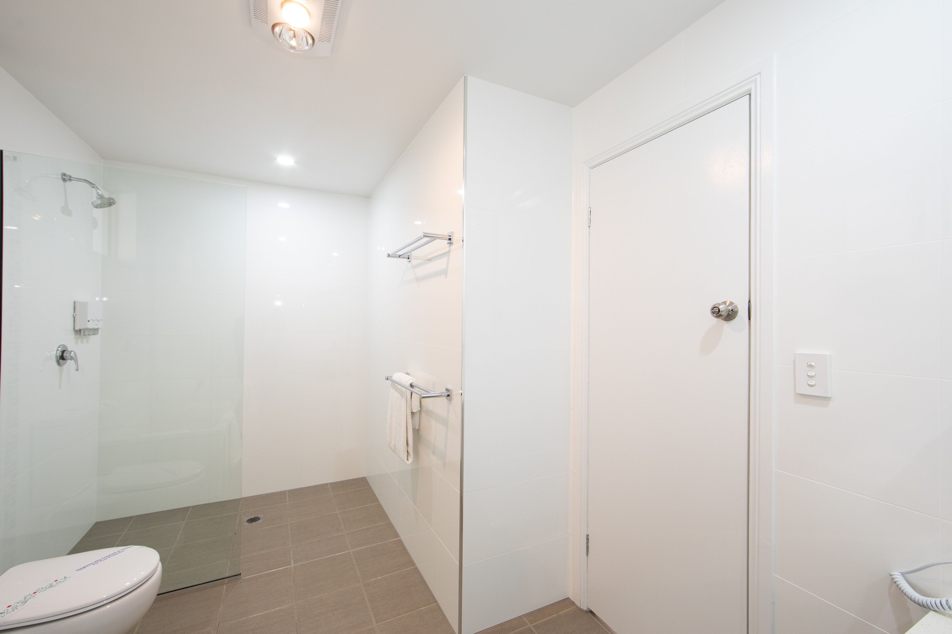 Une salle de bain moderne avec une douche à parois de verre, des toilettes et une porte blanche.