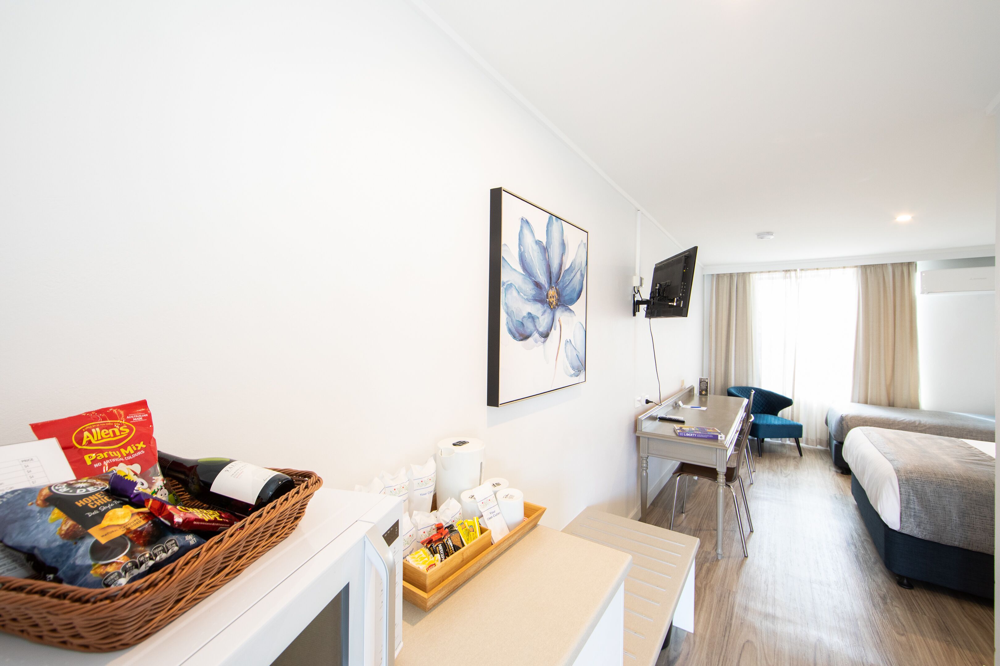 Une chambre d’hôtel équipée d’un bureau, d’un lit, d’une télévision et d’un plateau de petit-déjeuner avec des en-cas et une bouteille.