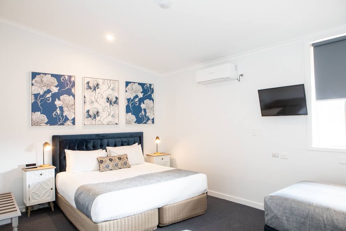 A modern bedroom with a large bed, bedside tables, a flat-screen TV, and artwork on the wall.