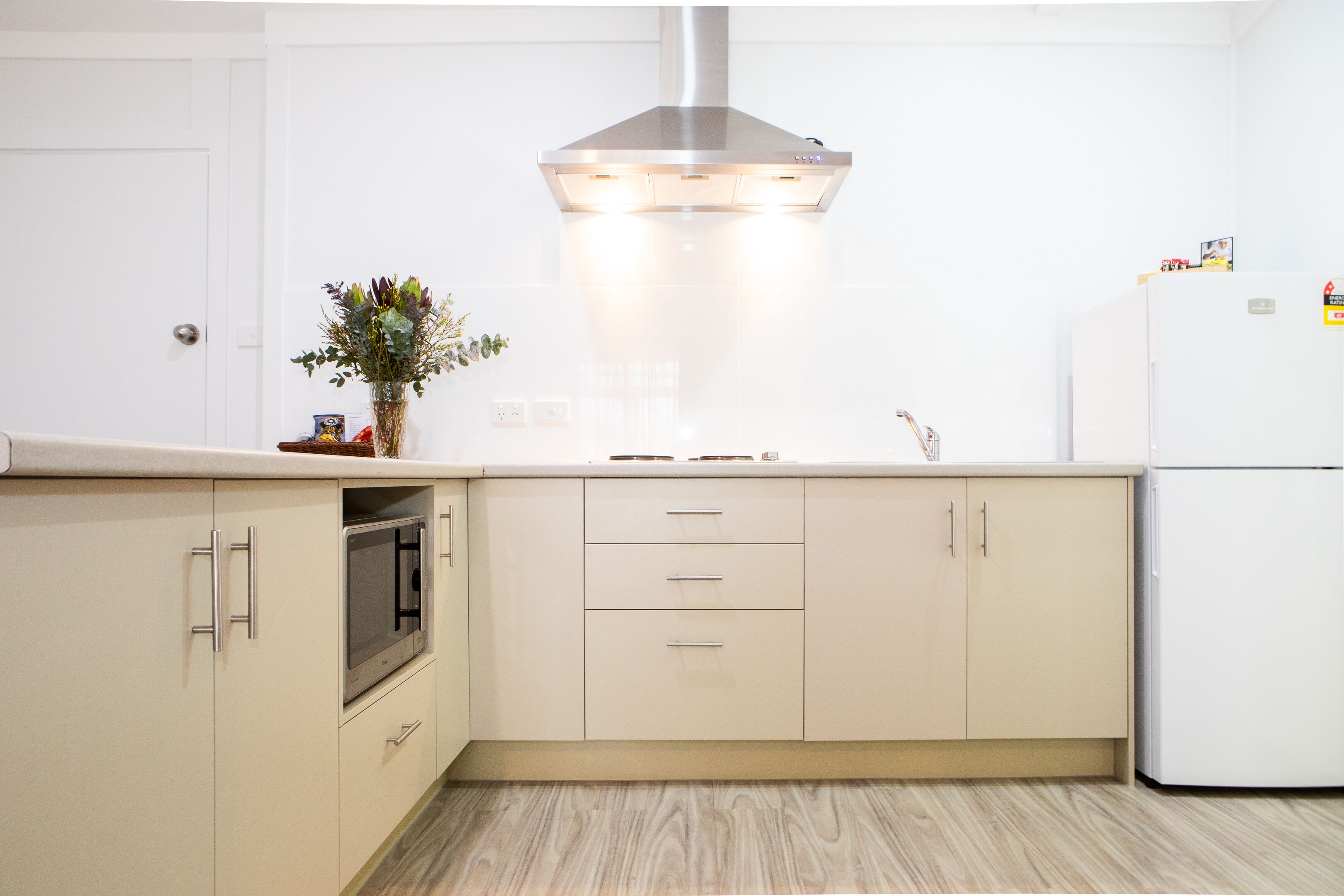A modern kitchen with white cabinets, a stainless steel range hood, and a white refrigerator.