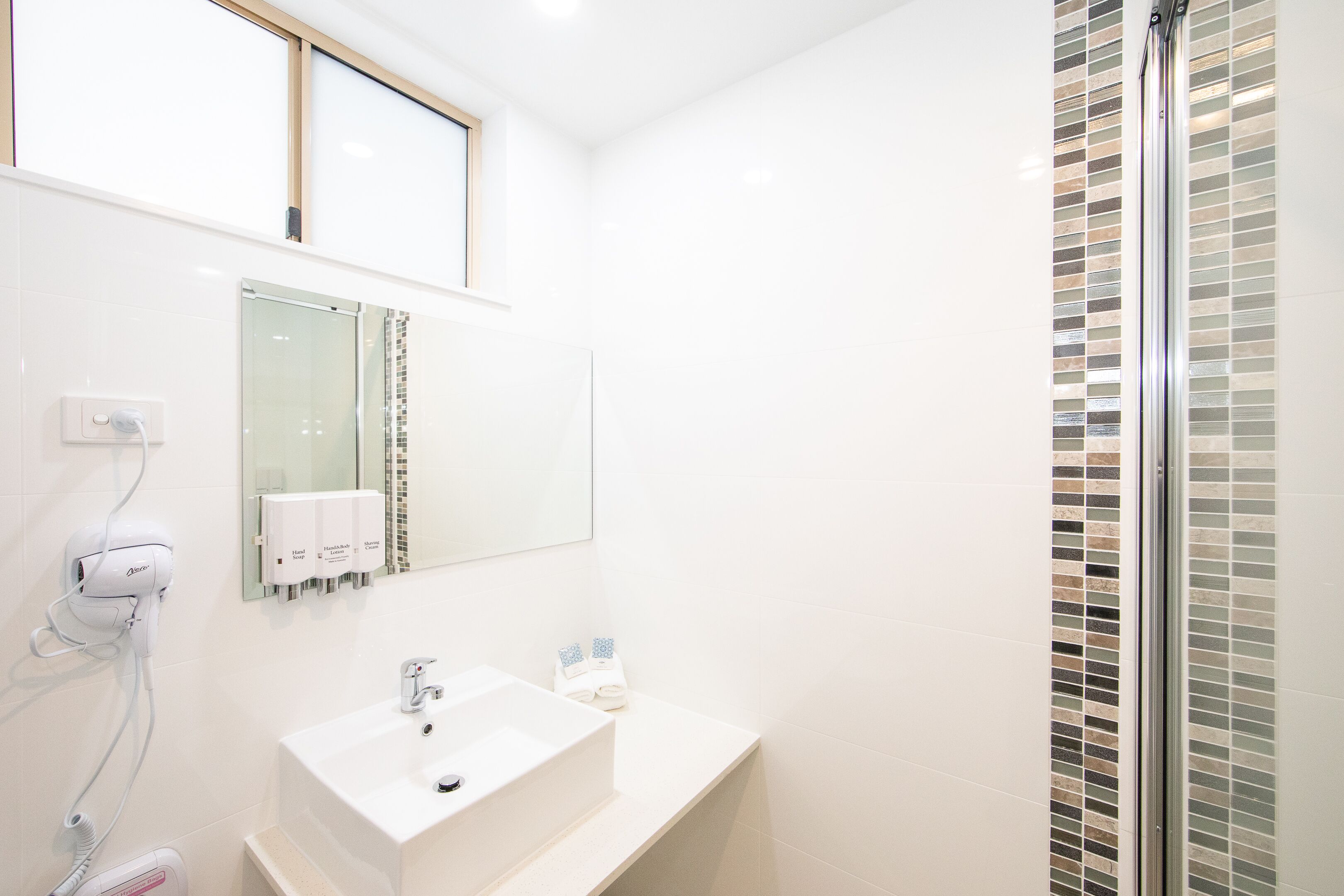 A modern bathroom with a white sink, a mirror, and a glass shower enclosure.