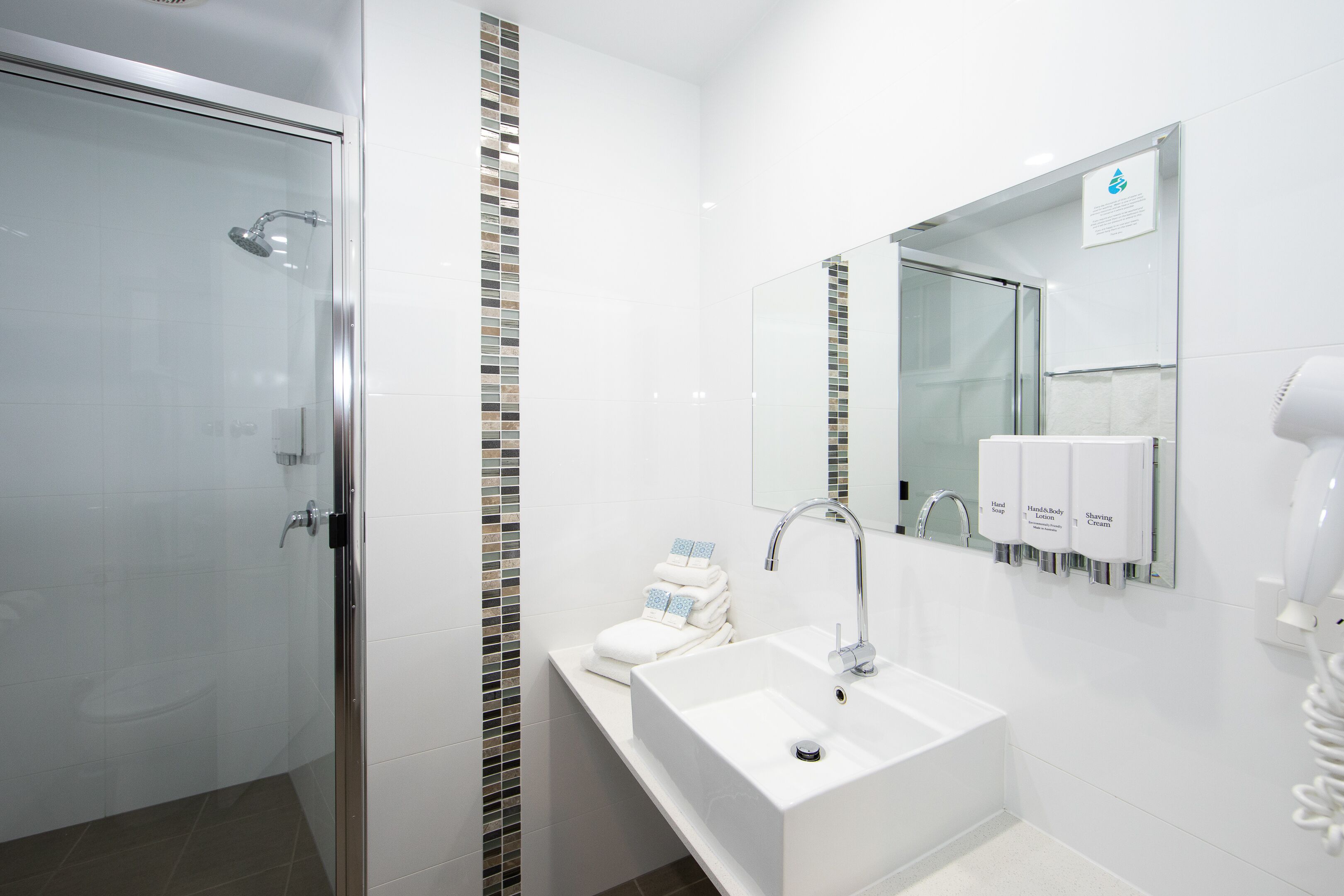 A modern bathroom with a glass shower enclosure, a white sink with a mirror, and hand soap dispensers.