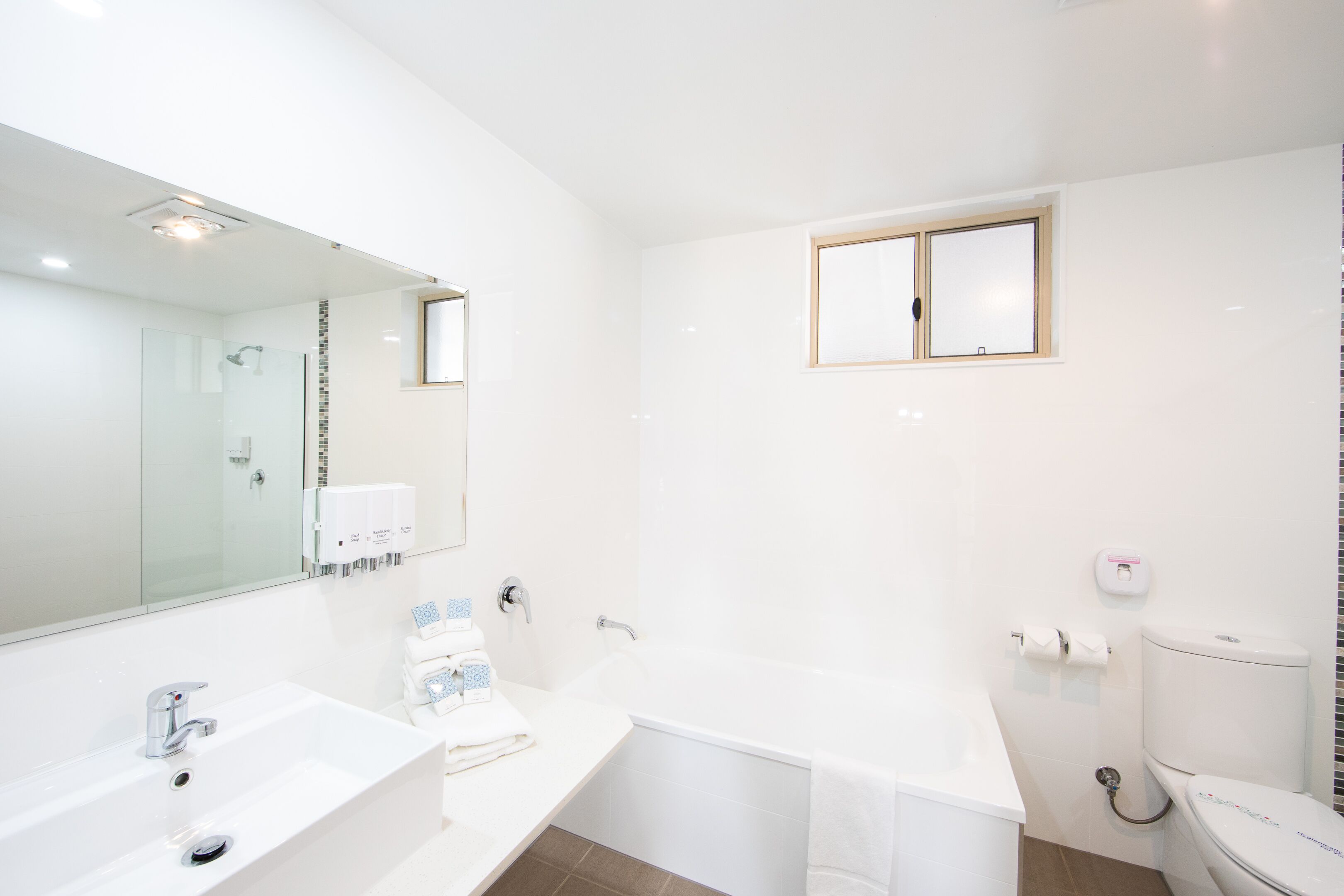 A modern bathroom with a large mirror, a sink, a bathtub, and a toilet.