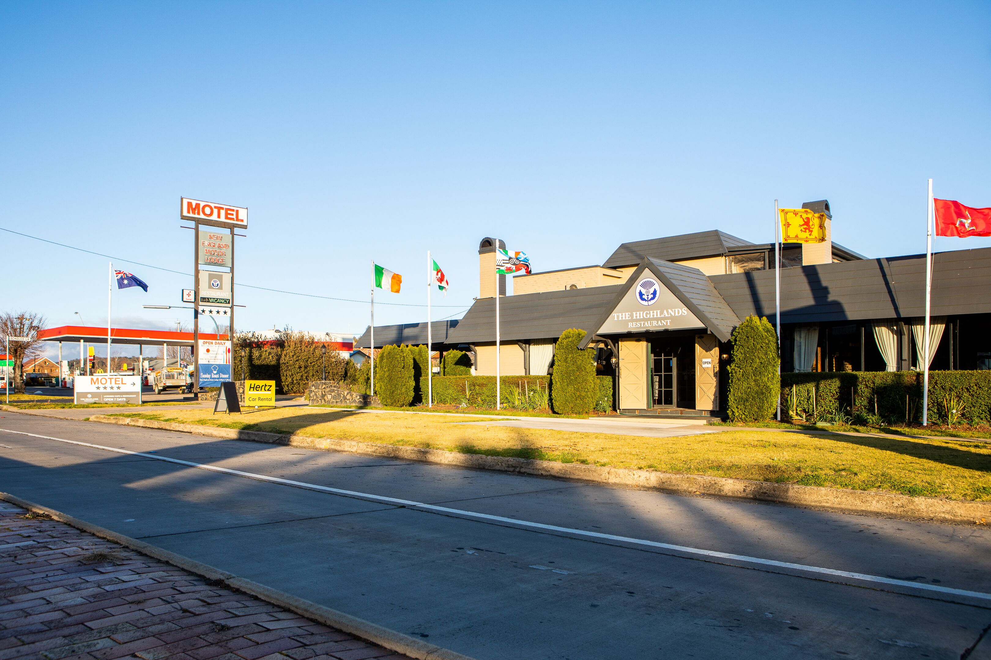 A motel with a signboard, flags, and a building with a sign for 'The Highlands Restaurant'.