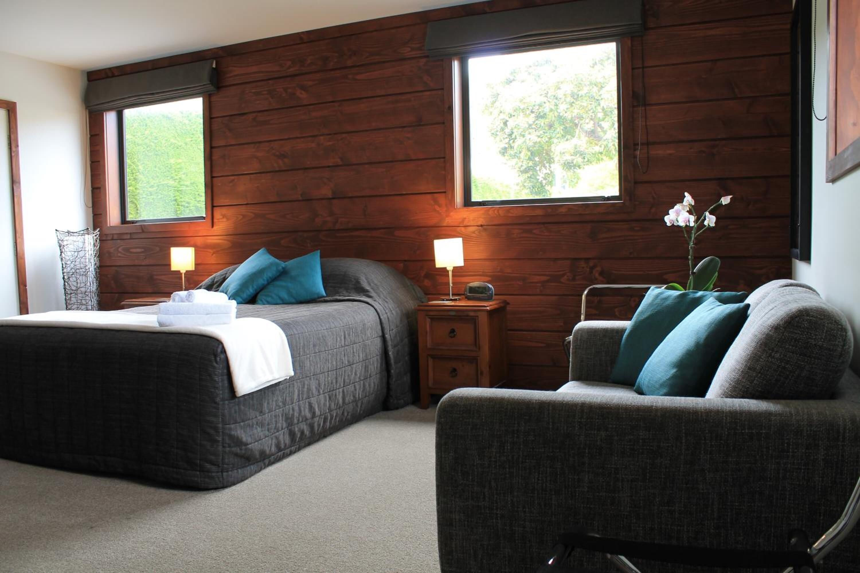 A bedroom with a bed, bedside tables, a chair, and two windows.