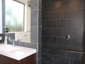 A modern bathroom with a white sink, dark tiles, and a window with a view. - Inn the Bay Bed & Breakfast (Kaikoura)