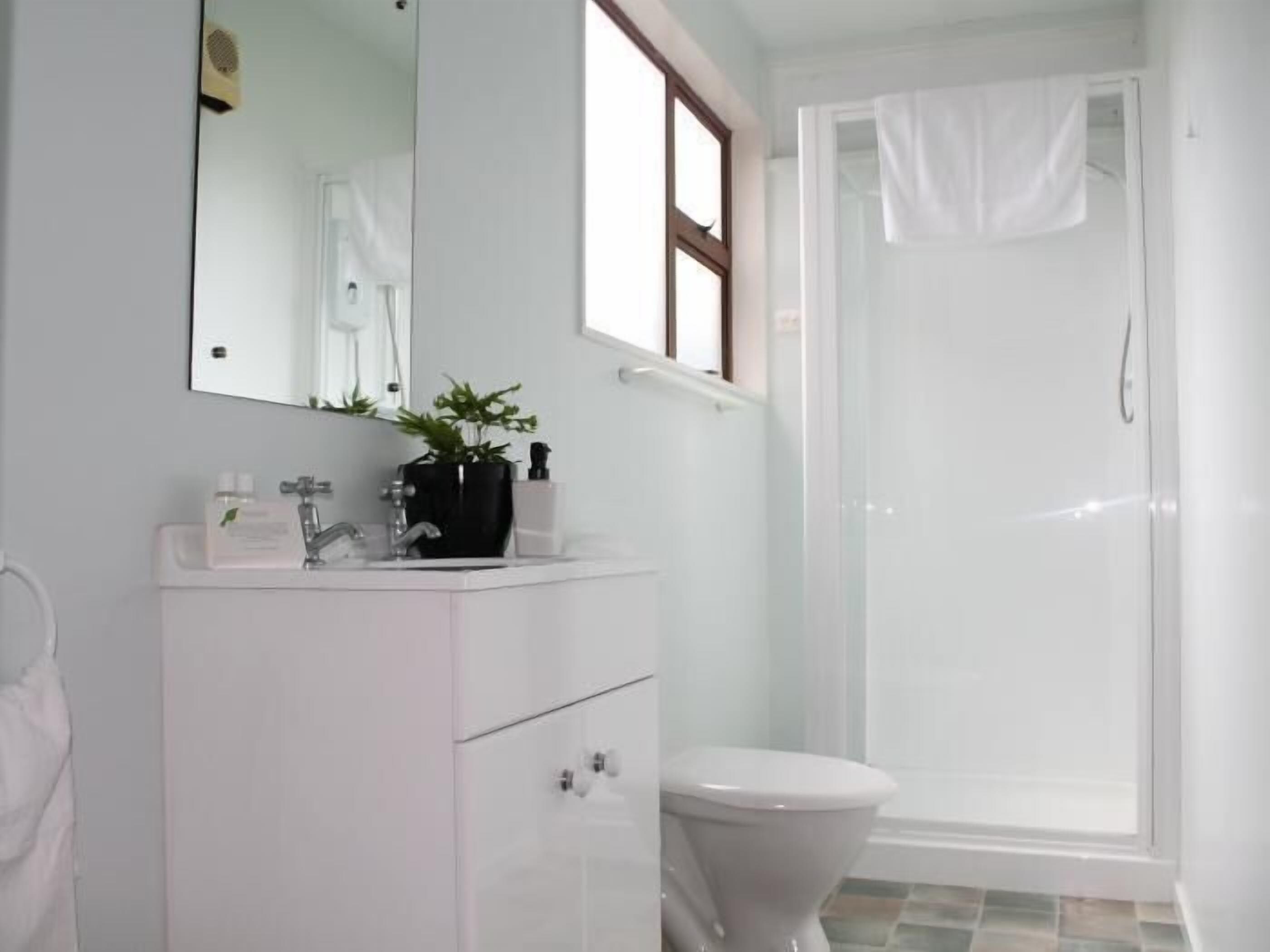 A bathroom with a white sink, mirror, and toilet. There is a window above the sink and a shower area with a glass door.
