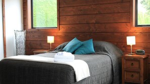 A bedroom with a large bed, two bedside tables with lamps, and a view of greenery through the window. - Inn the Bay Bed & Breakfast (Kaikoura)