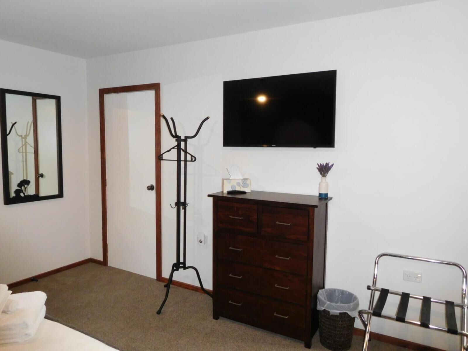 A bedroom with a wooden dresser, a coat rack, a television, and a trash can.