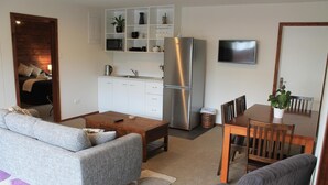 A modern living room with a sofa, coffee table, and dining table. A kitchen area with a refrigerator and microwave is visible. - Inn the Bay Bed & Breakfast (Kaikoura)
