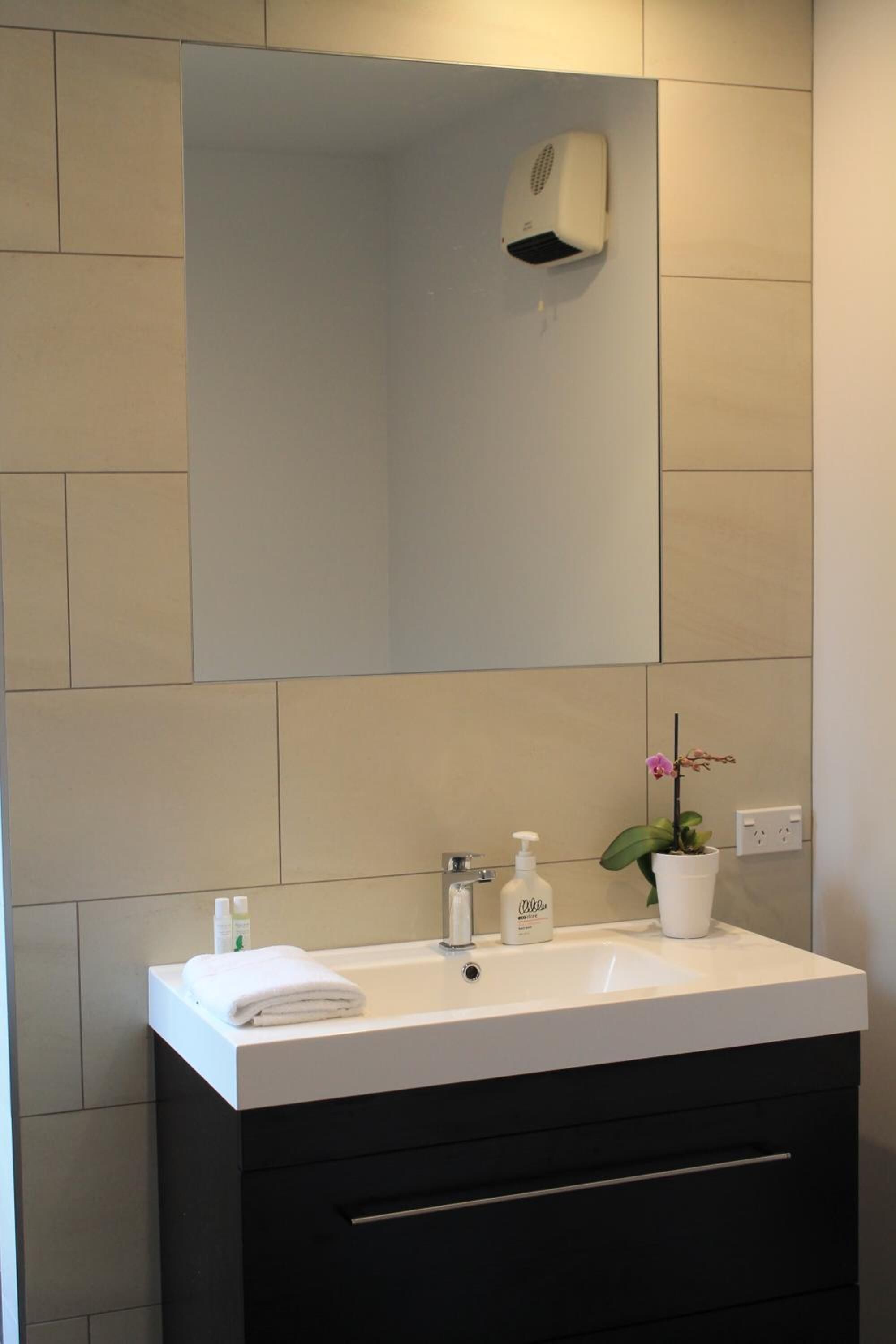Un baño moderno con lavamanos blanco, armarios negros, un espejo y un cabezal de ducha manual.