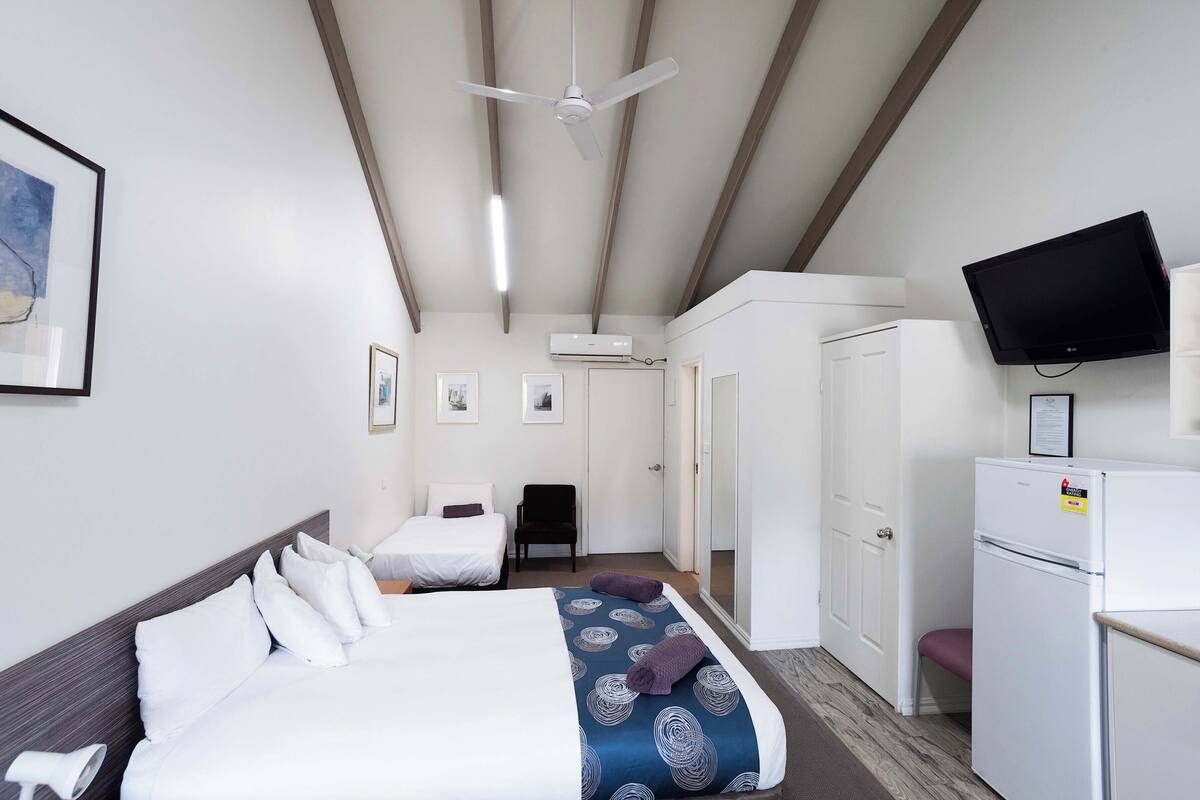 A hotel room with a bed, a desk, a chair, a television, and an air conditioning unit.