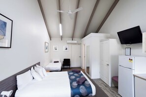 A hotel room with a bed, a desk, a chair, a television, and an air conditioning unit. - Canberra Ave Villas (Queanbeyan)