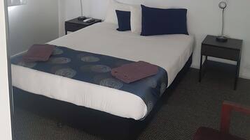 A hotel room with a bed, two bedside tables, a lamp, a framed picture of a parrot, and a chair.