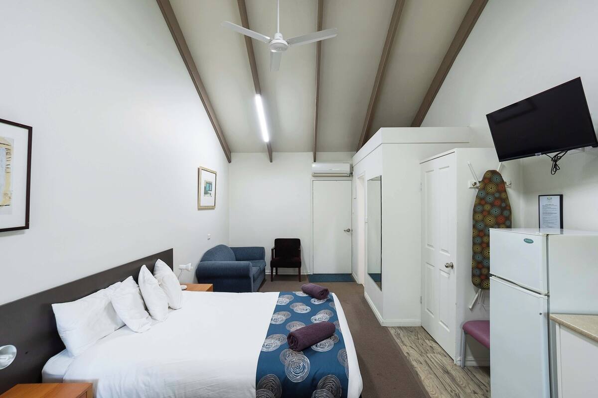 A hotel room with a bed, a desk, a chair, a television, and a wardrobe.