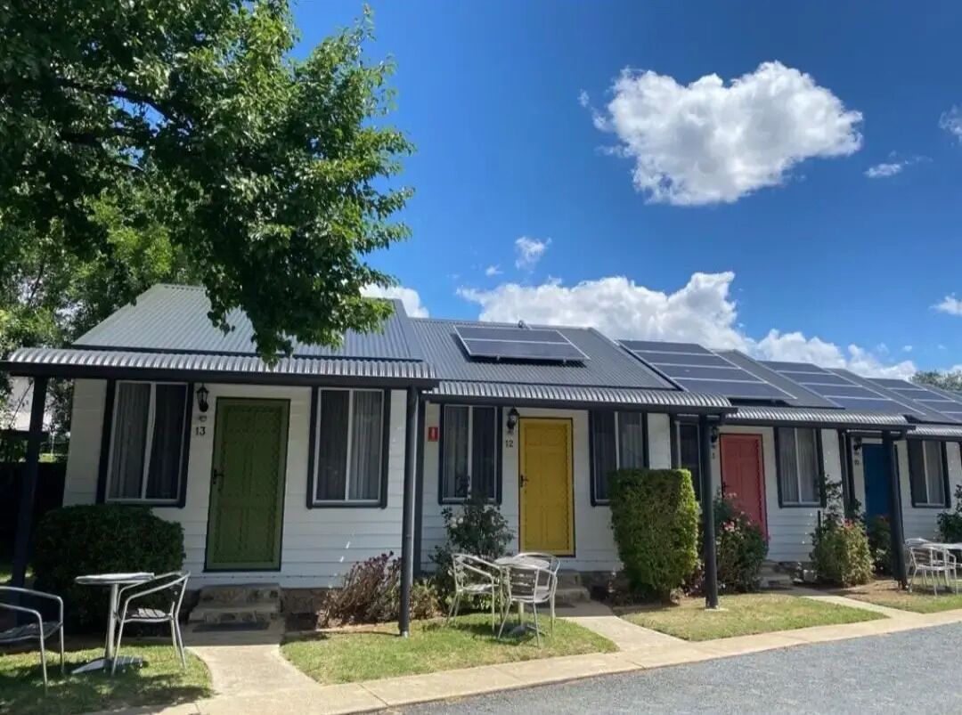 Een rij mobiele woningen met zonnepanelen op de daken, elk met een andere deurkleur.