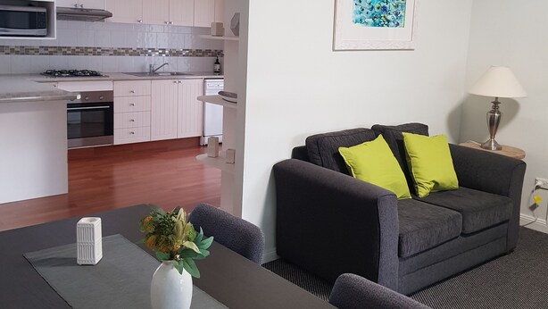 A modern living space with a dining area, a kitchen, and a gray sofa with green cushions. - Canberra Ave Villas (Queanbeyan)