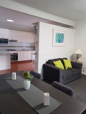 A modern living space with a dining area, a kitchen, and a gray sofa with green cushions. - Canberra Ave Villas (Queanbeyan)