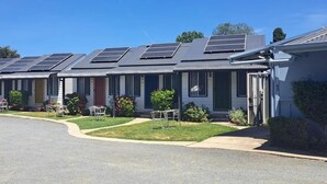 A row of single-story buildings with solar panels on the roofs, outdoor seating, and a well-maintained lawn. - Canberra Ave Villas (Queanbeyan)