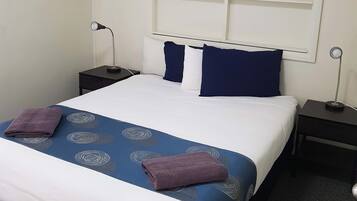 Een hotelkamer met een groot bed, twee nachtkastjes, een wandplank en een klein bureau.